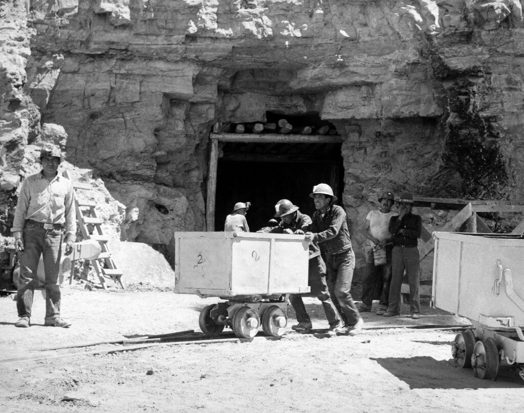 A photograph depicting uranium mining during the nuclear age. Workers are seen operating heavy machinery and tools in a rocky landscape to extract uranium, a critical resource for nuclear weapons and energy.