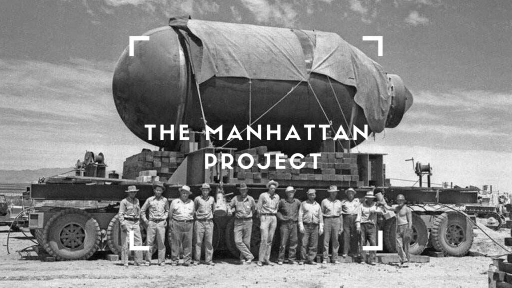A historical black-and-white photograph of Manhattan Project male workers standing together in front of the assembled atomic bomb.